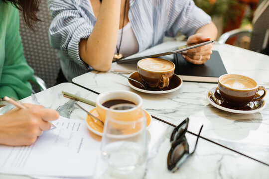 Two young women discussing work processes, signing documents and drinking coffee at a cafe