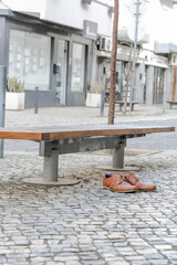 Brown leather shoes on a cobblestone pavement next to a bench in an urban setting