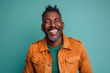 Fototapeta premium Portrait of a grinning afro-american man in his 40s wearing a trendy bomber jacket in front of pastel teal background