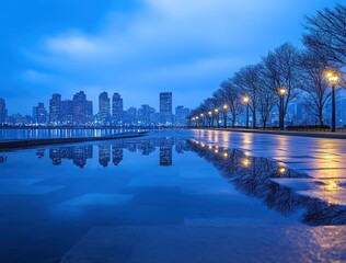 A serene cityscape at dusk, featuring reflections on a wet path alongside a river.