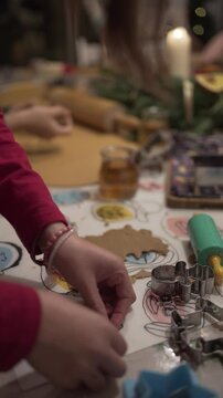vertical detail video of child's hands kneading and shaping gingerbread biscuit with red colours and christmas ornaments
