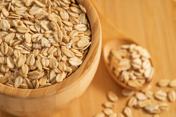 Rolled oats in a wooden bowl and spoon on a bamboo surface. Perfect for healthy eating and natural food themes.