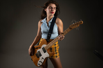 Cool young woman playing electric guitar on grey background