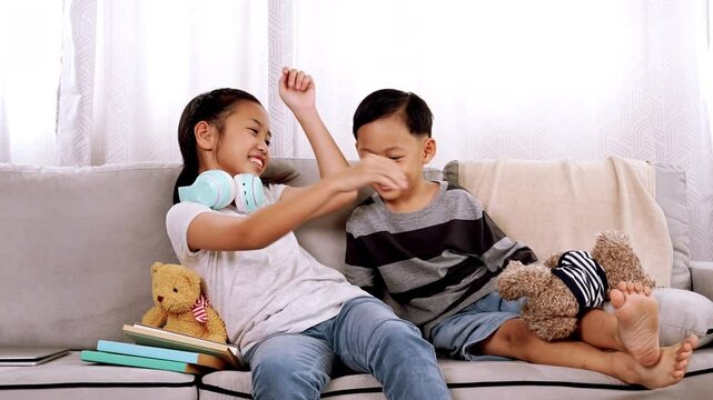 Little brother run to sister, eager to play with her while she using laptop. Sister playfully pinched brother's cheeks embracing and kiss his younger brother in living room Both siblings look happy 