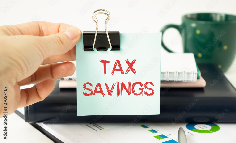 Poster a sheet of paper with the text tax savings in hand on the background of a calculator and alarm clock