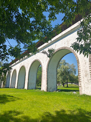 A view of a historic aqueduct featuring multiple arches, set against modern city buildings and lush greenery