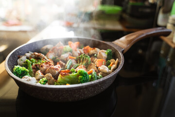 Culinary at home. Fresh green vegetables and chicken on a frying pan on an induction stove in a kitchen. Close up of food for meat eaters. Homemade food. Nutrition and a healthy lifestyle.
