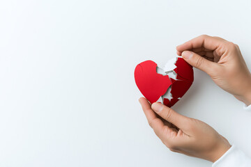 pair of hands gently holds broken heart shaped paper, symbolizing emotional pain and heartbreak. contrasting colors evoke feelings of sadness and loss