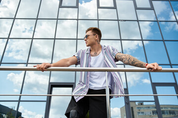 A young man with a prosthetic leg stands on a balcony enjoying the view and sunlight.