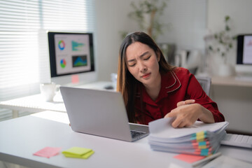 Stressed businesswoman suffering from headache while working with laptop computer and financial documents at office desk, feeling tired and overworked