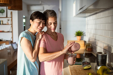 Lesbian couple making healthy organic smoothie together in modern kitchen