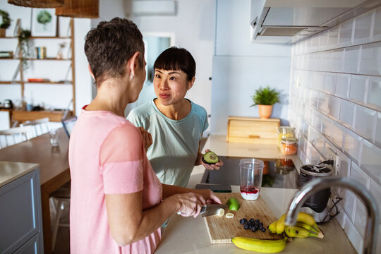 Lesbian couple making healthy organic smoothie together in modern kitchen - Powered by Adobe
