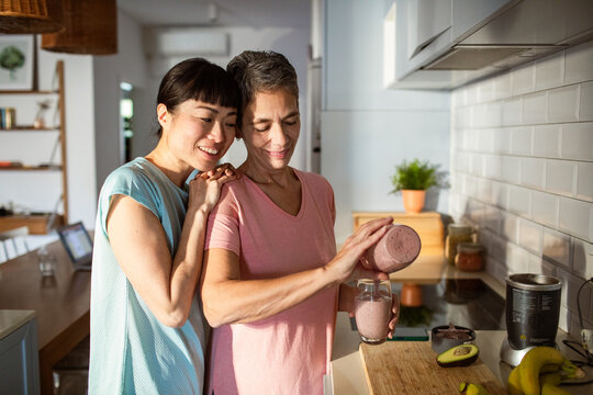 Lesbian couple making healthy organic smoothie together in modern kitchen - Powered by Adobe