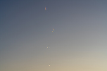 Four aircraft flying in sky trailing reflected orange vapour trails from early morning sunrise