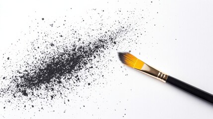 A paintbrush rests beside a pile of black powder on a white surface, suggesting an artistic or creative process.
