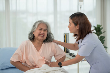 Asian nurse helping a senior Asian female patient with stomach ache on a bed in hospital