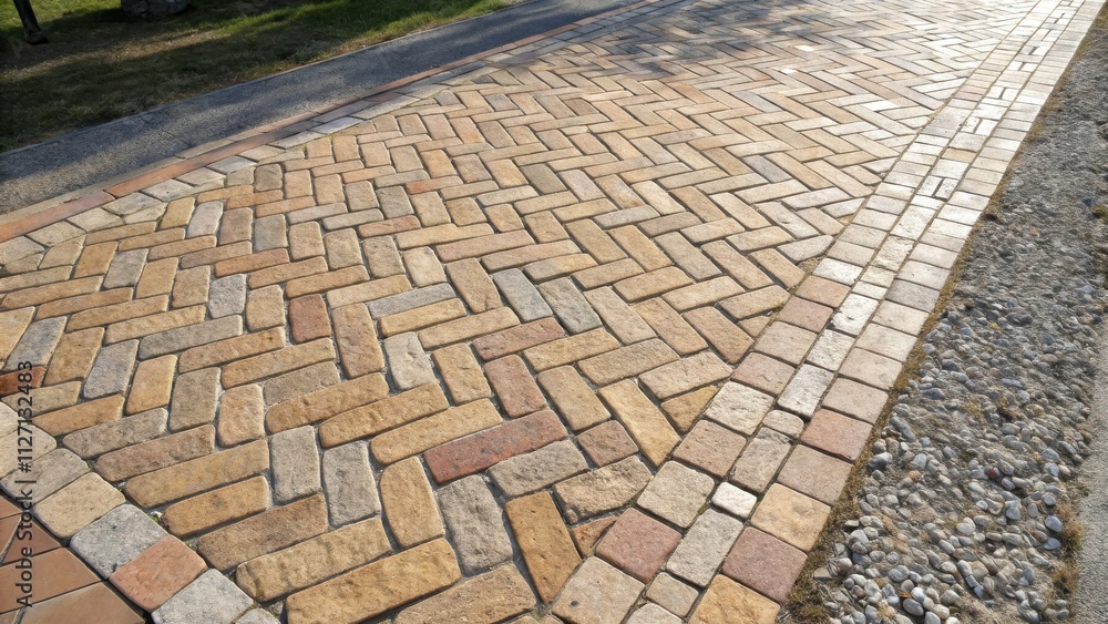 Leinwandbilder a herringbone pattern of brick pavers create a pathway bordered by a row of stones and a strip of gr