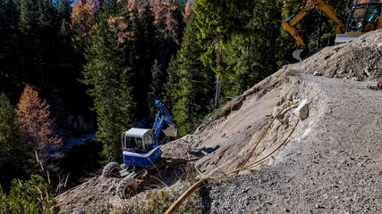 Construction equipment stabilizes a steep hillside in a forested area, highlighting erosion control...