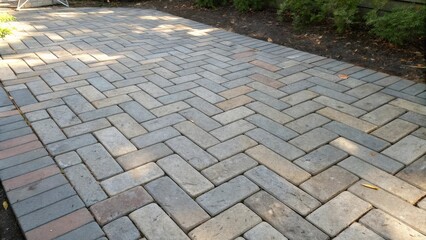 Fototapeta premium A herringbone pattern of gray, tan, and red bricks creates a walkway lined with lush greenery.