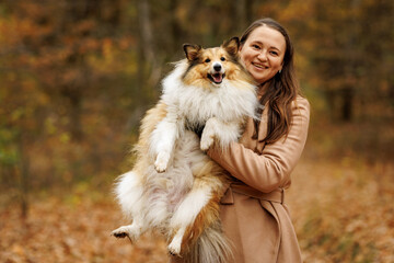 A woman joyfully holding her adorable collie dog amidst a beautiful autumn forest