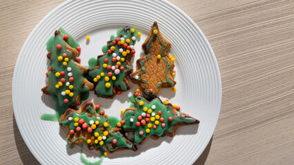 Colorful Christmas tree-shaped cookies with green icing and sprinkles on a white plate, celebrating festive holiday baking traditions