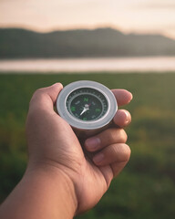 Hands holding a compass pointing the direction with a lake and mountains in the background at sunset. 