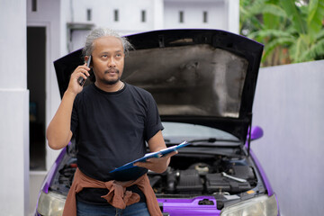 Indonesian male mechanic reports the results of the car's roadworthiness check via voice call, an automotive industry concept.