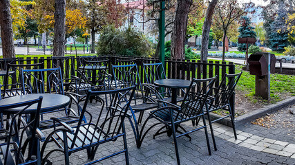 Empty outdoor cafe chairs and tables under autumn trees highlight social distancing challenges during fall gatherings