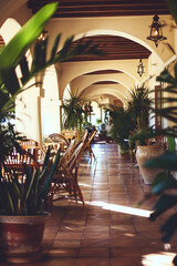 interior of restaurant or hotel with a Mexican or tropical aesthetic . Archways, stucco, clay tile and lush potted  plants surround tables in an open indoor outdoor rustic luxury patio space.