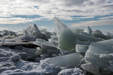 Broken ice close-up - hummocks on the Baltic Sea coast in winter. Beautiful low cloudy sky, side backlight natural yellow sunlight at the end of a short winter day © Alexander Korotkov