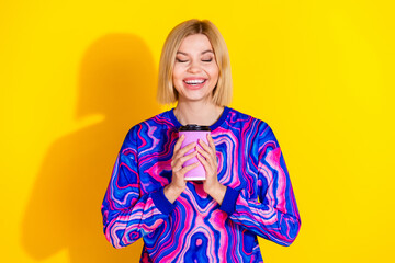 Photo portrait of pretty young girl smell aroma coffee hold paper cup wear trendy colorful blue outfit isolated on yellow color background