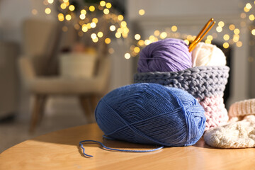 Colorful yarns, knitted mittens and crochet hooks on wooden table indoors, closeup. Space for text