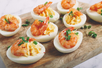 Boiled eggs stuffed with yolk and seasoned with mayonnaise, stuffed eggs with shrimp, on a wooden chopping board, selective focus, close-up, no people,