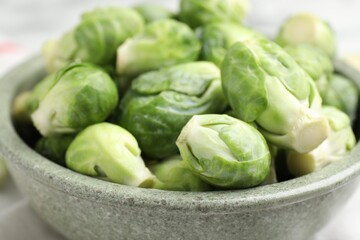 Fresh Brussels sprouts in bowl on white table, closeup