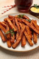 Delicious sweet potato fries, parsley and sauce on beige textured table, closeup