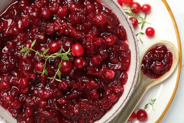 Tasty cranberry sauce in bowl, berries, thyme and spoon on table, top view