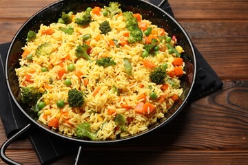 Tasty rice with vegetables in baking dish on wooden table, closeup