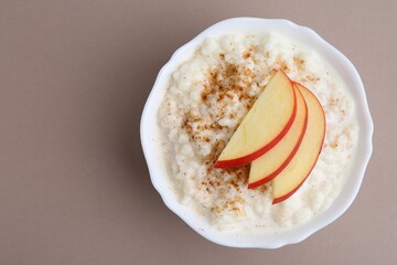 Delicious rice pudding with cinnamon and apple on dark beige background, top view. Space for text