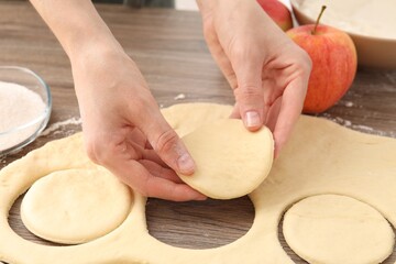 Woman making pirozhki (stuffed pastry pies) at wooden table, closeup