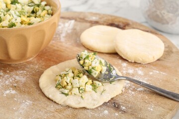 Making pirozhki (stuffed pastry pies). Pieces of dough with eggs and dill filling on table, closeup