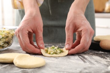 Woman making pirozhki (stuffed pastry pies) with eggs and dill at gray table indoors, closeup