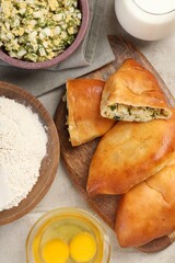 Delicious pirozhki (stuffed pastry pies) and ingredients on grey table, flat lay