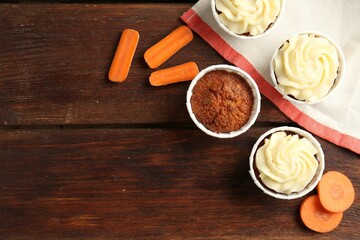 Delicious carrot muffins and fresh vegetables on wooden table, flat lay. Space for text