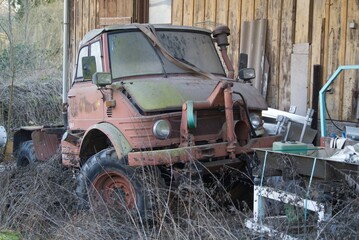 A very old commercial vehicle stands next to a wooden wall