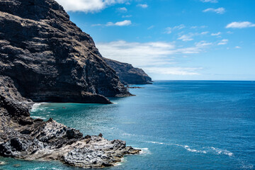 The image shows steep, rugged cliffs descending into a calm, blue ocean. The cliffs contrast with...