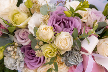 Beautiful close-up of a flower bouquet featuring lavender, white, and pale yellow roses, complemented by lush greenery and delicate ribbon accents. Perfect for wedding themes, floral arrangements, and