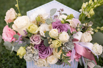 A stunning flower arrangement featuring lavender, white, pink, and pale yellow roses, elegantly arranged in a decorative gift box with ribbons, set on lush green grass. Perfect for weddings, romantic
