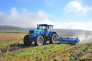 Obraz premium Blue tractor plowing field in idyllic rural landscape with rolling hills.