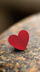 Fototapeta premium A red heart cutout rests on a stone surface, representing emotional pain during Valentine's Day. The backdrop is a stark black, emphasizing the heartbreak theme