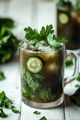 Fototapeta premium Refreshing drink with cucumber and herbs in a glass, garnished with ice and greenery.
